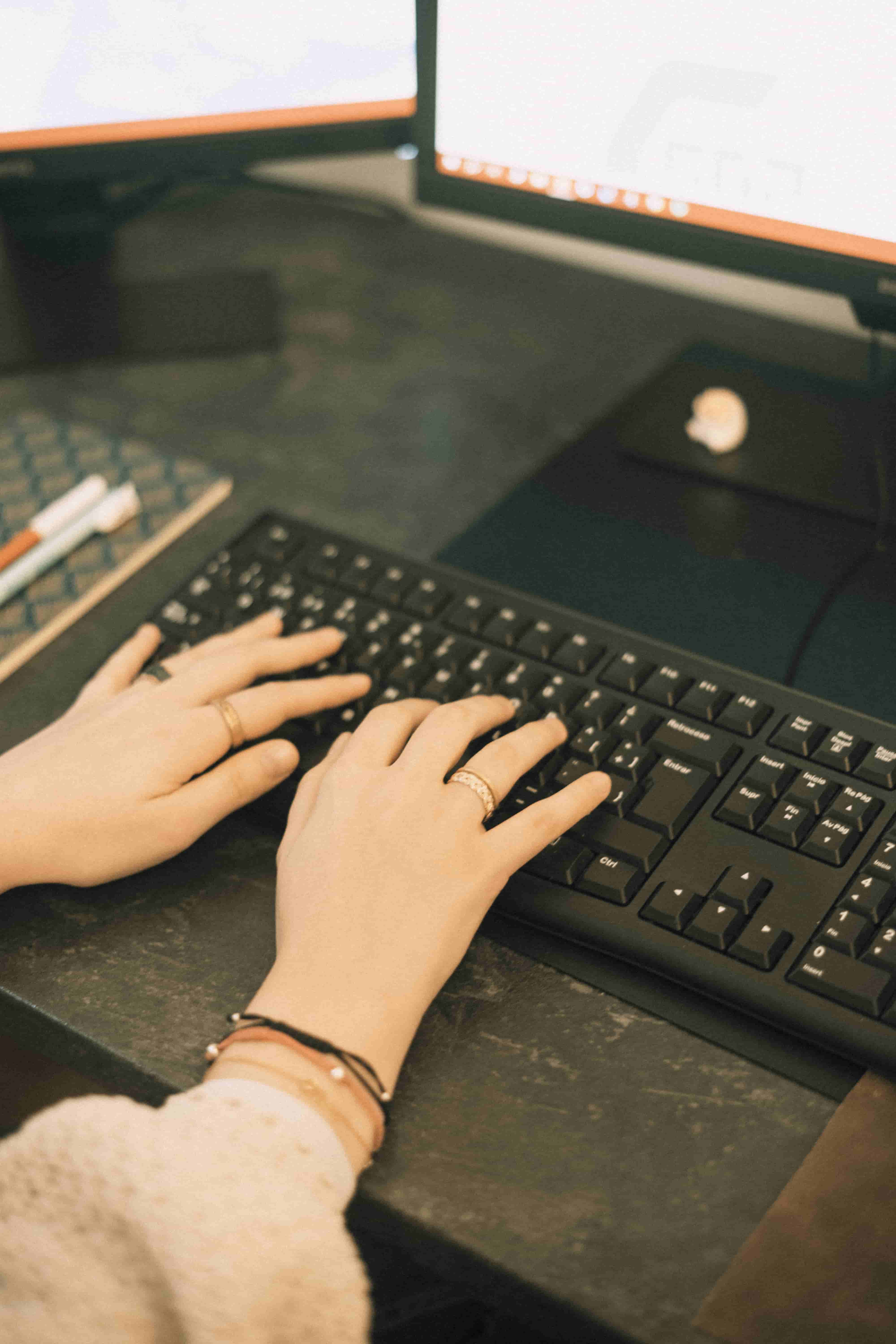 Dos manos de mujer escriben en un teclado de ordenador junto a una agenda