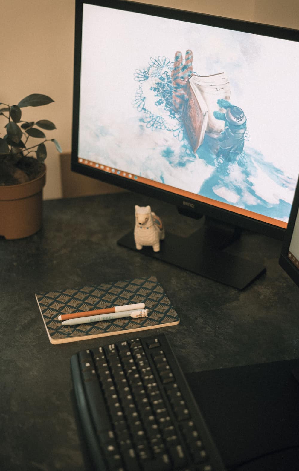 Close-up shot of a computer screen next to a keyboard, a mouse, a planner, two pens, a toy llama, and a plant