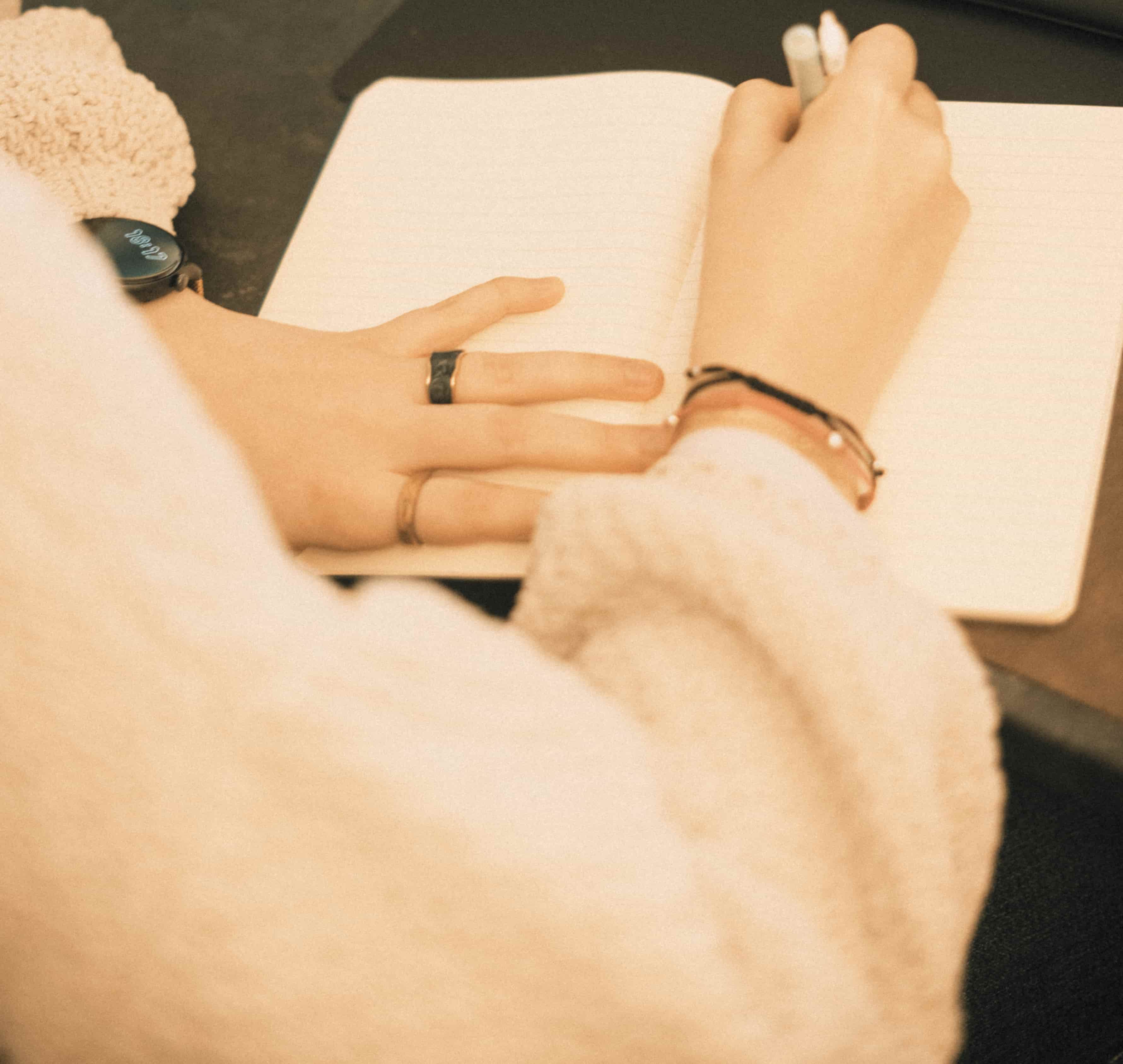 Una mano de mujer escribe en una agenda mientras apoya la otra mano sobre el papel