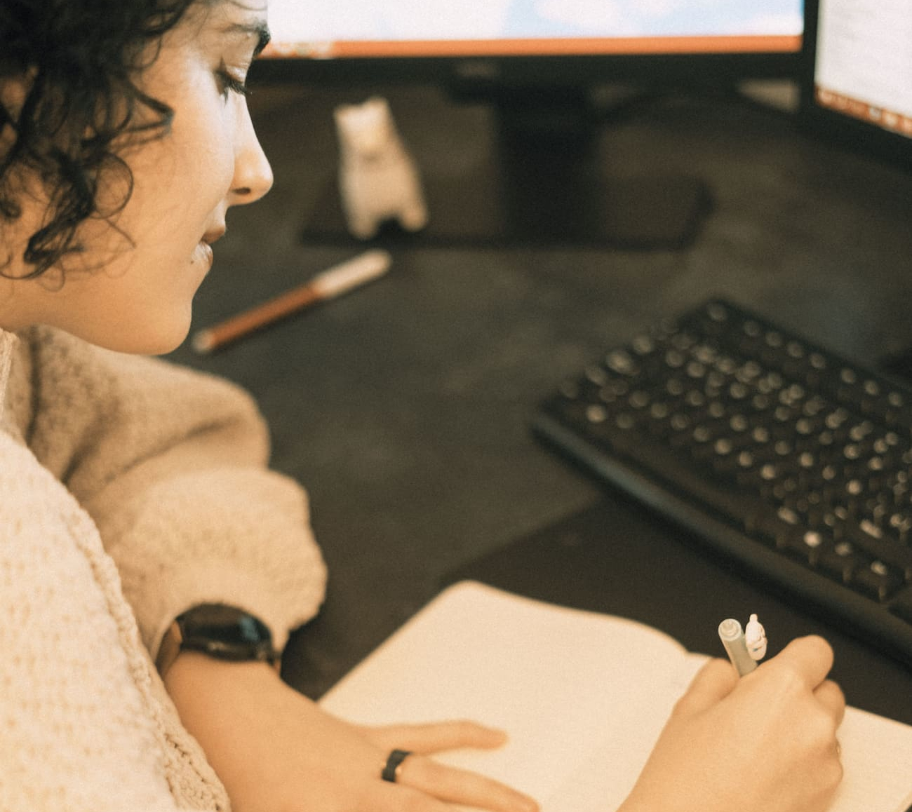 A woman is writing with a pen on a planner next to a computer keyboard