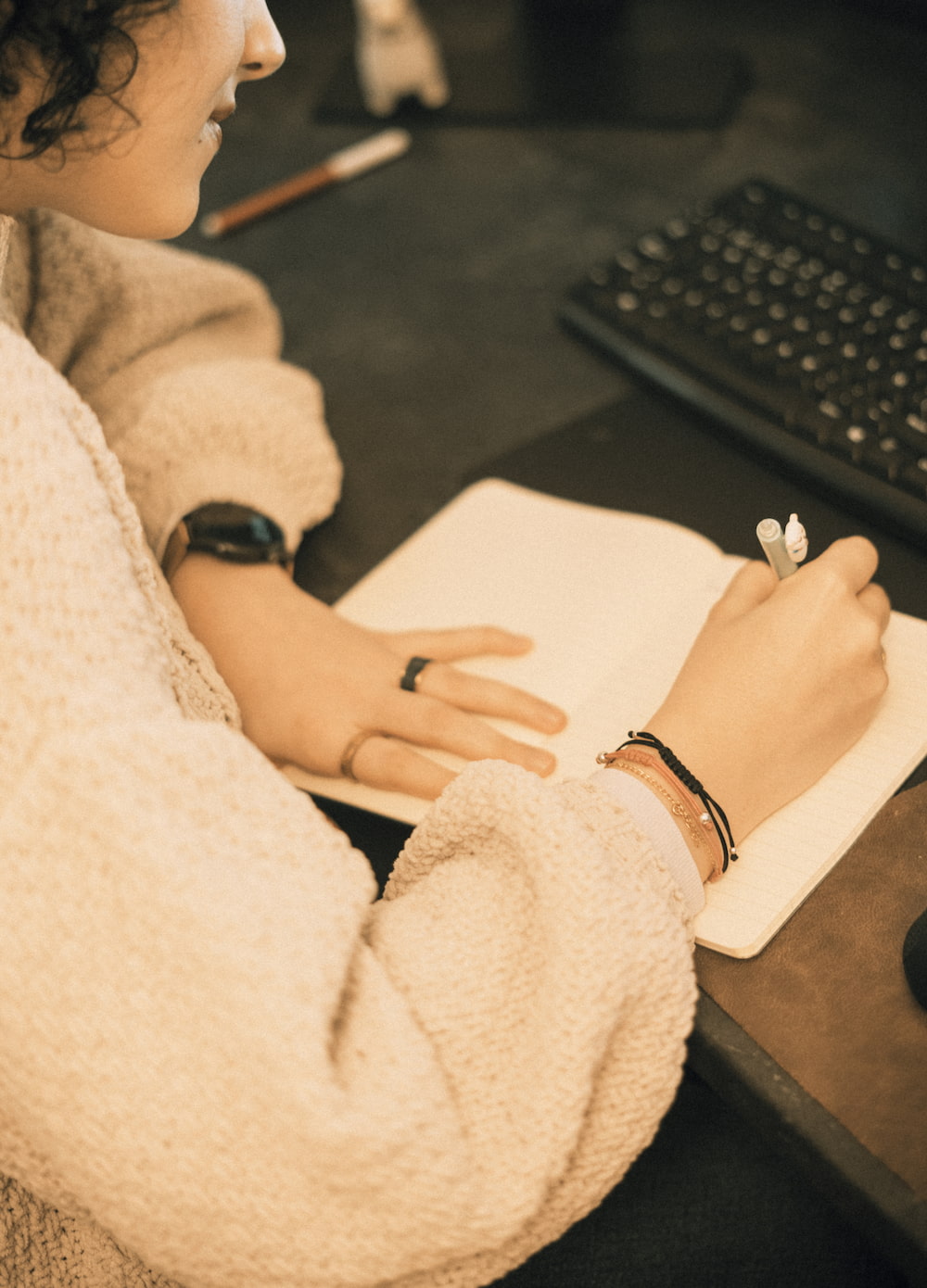 Close-up shot of a woman jotting down ideas with a pen on a notebook next to a keyboard
