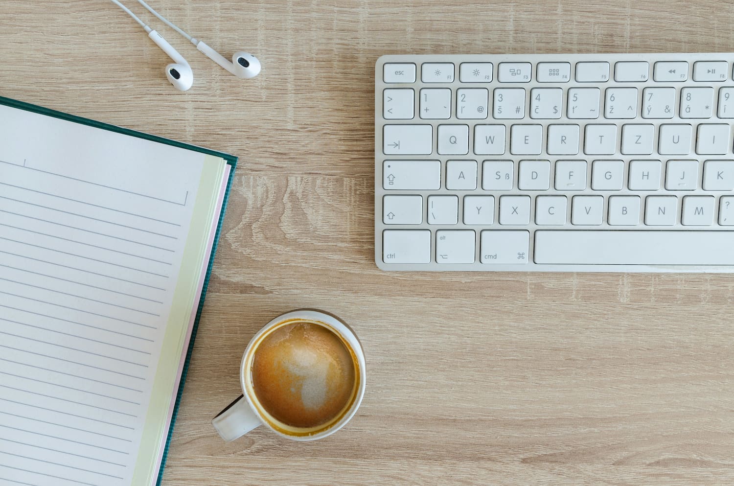 Overhead shot of a desk with a computer keyboard, a headset, a planner and a coffee mug